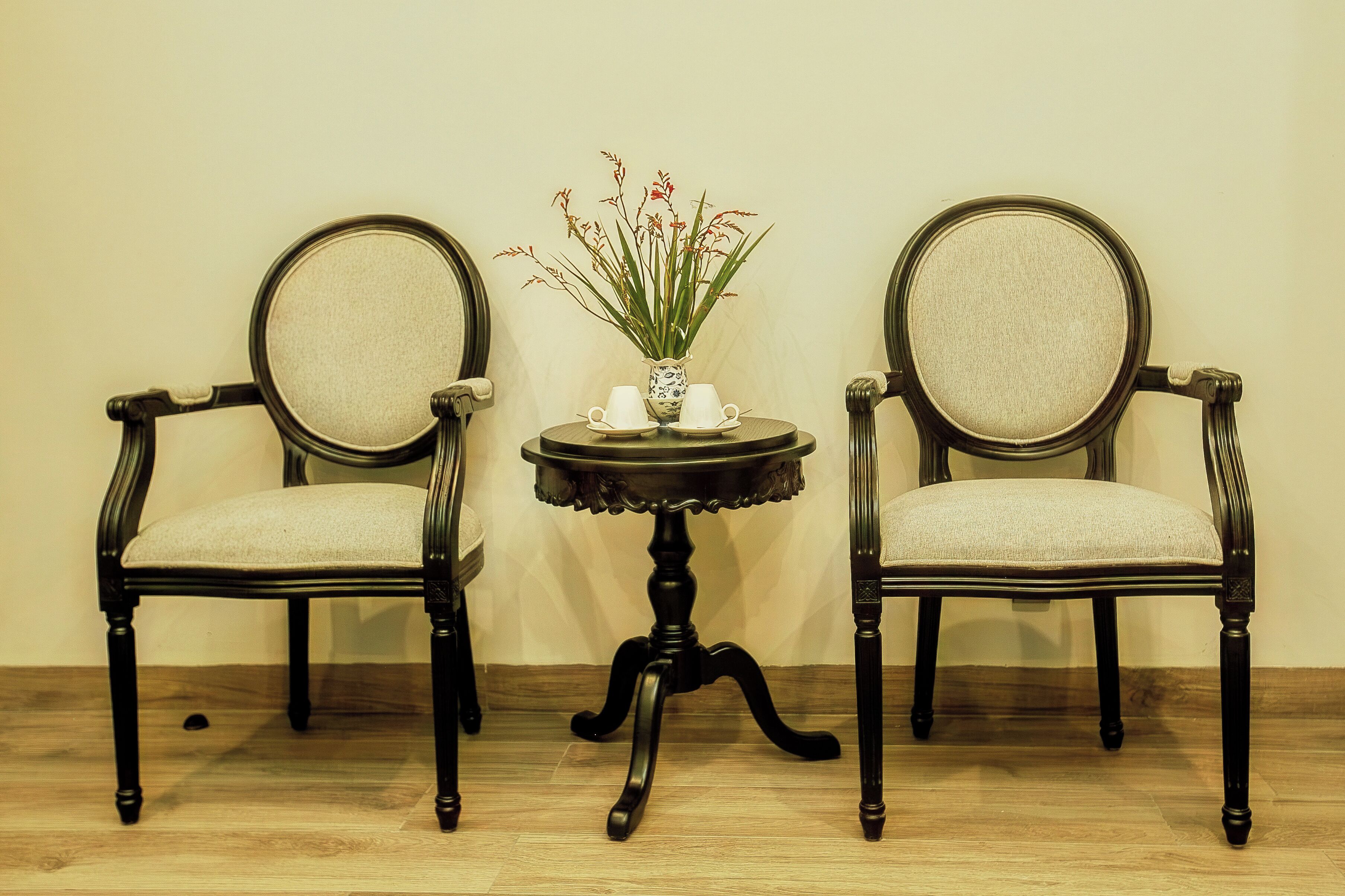 Deux chaises de style ancien, dotées d’assises et de dossiers rembourrés, sont placées de part et d’autre d’une petite table ronde sur laquelle se trouve un vase de fleurs.