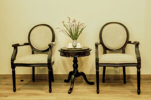 Two antique-style chairs with cushioned seats and backs, positioned on either side of a small round table with a vase of flowers.