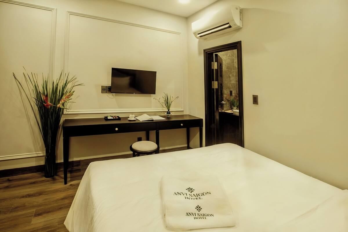 A hotel room with a bed, a desk, a chair, a flat-screen TV, a mirror, and a potted plant.