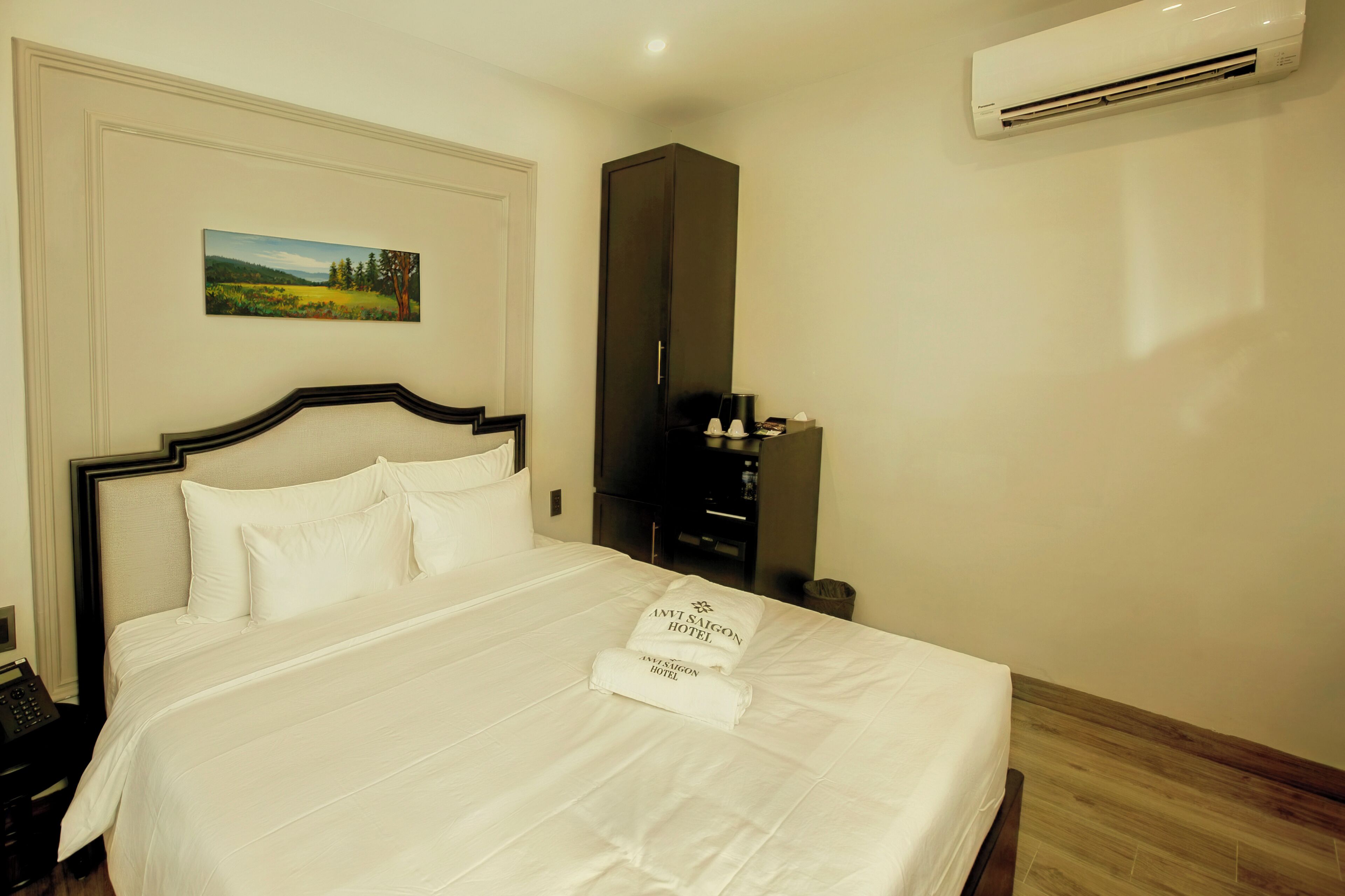 A hotel room with a bed, a painting, a wardrobe, and an air conditioner.