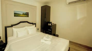 A hotel room with a bed, a painting, a wardrobe, and an air conditioner.