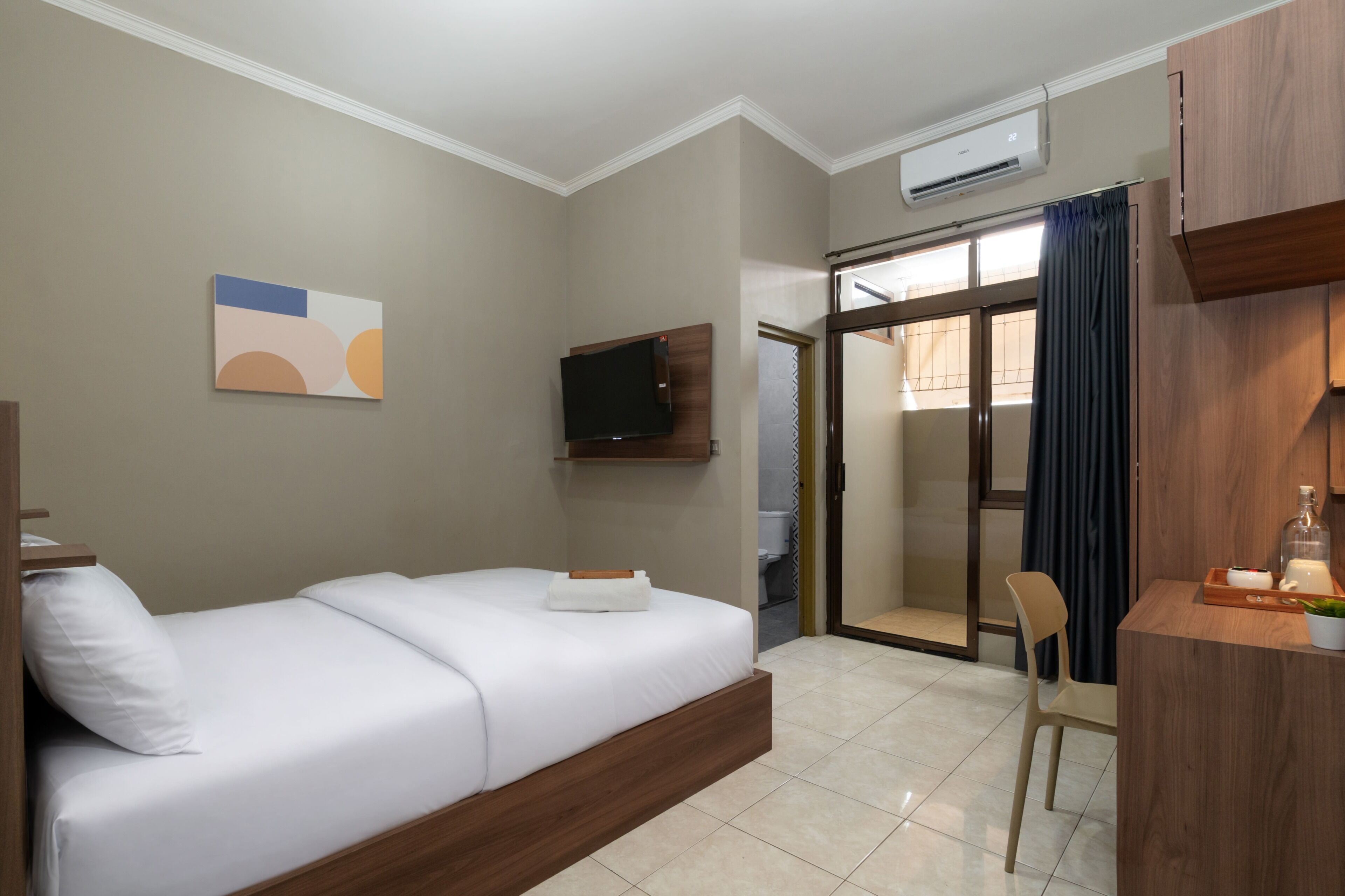 A hotel room with a bed, a TV, a desk with a chair, and a sliding door leading to a bathroom.