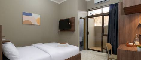 A hotel room with a bed, a TV, a desk with a chair, and a sliding door leading to a bathroom.