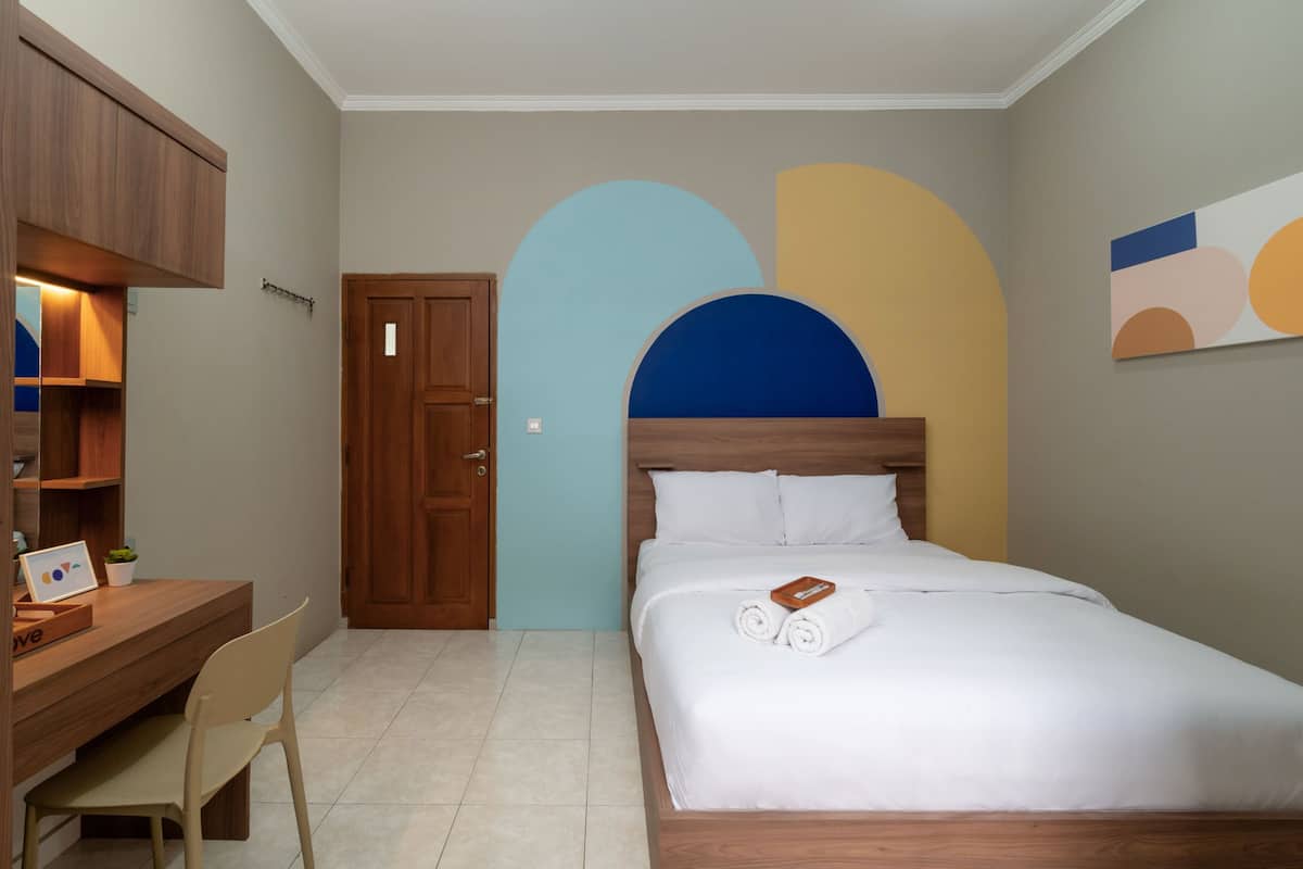 A bedroom with a wooden desk, chair, and bed with rolled towels.