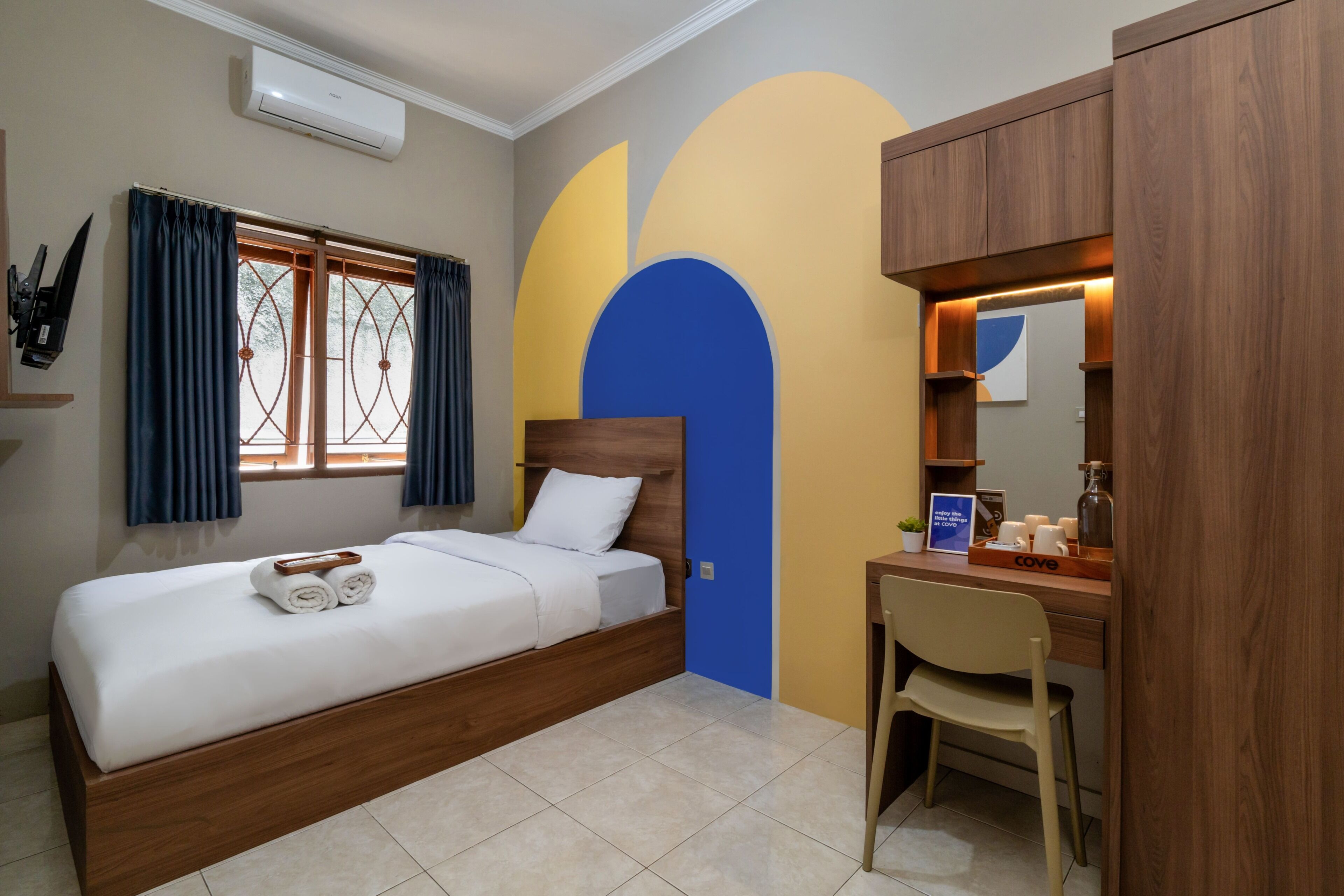 Una habitación de hotel con cama, escritorio, silla y ventana con cortinas.