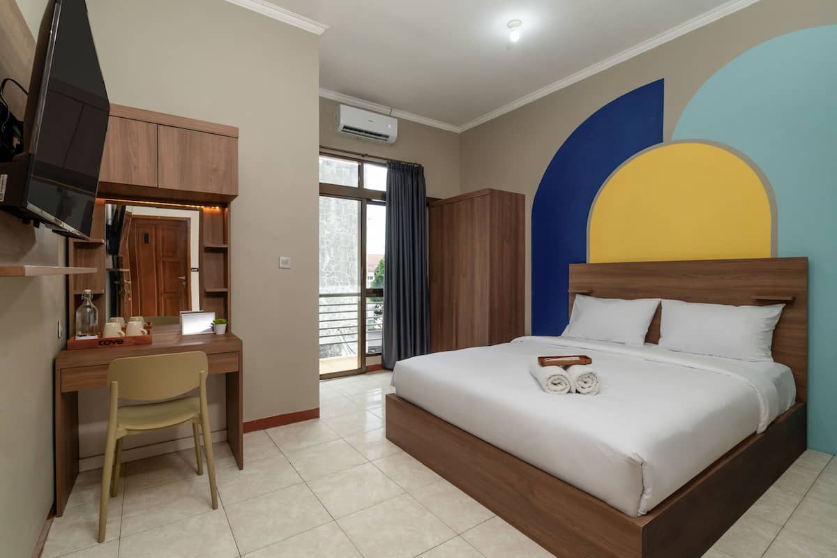 A hotel room with a bed, a desk with a chair, a television, and a window with curtains.