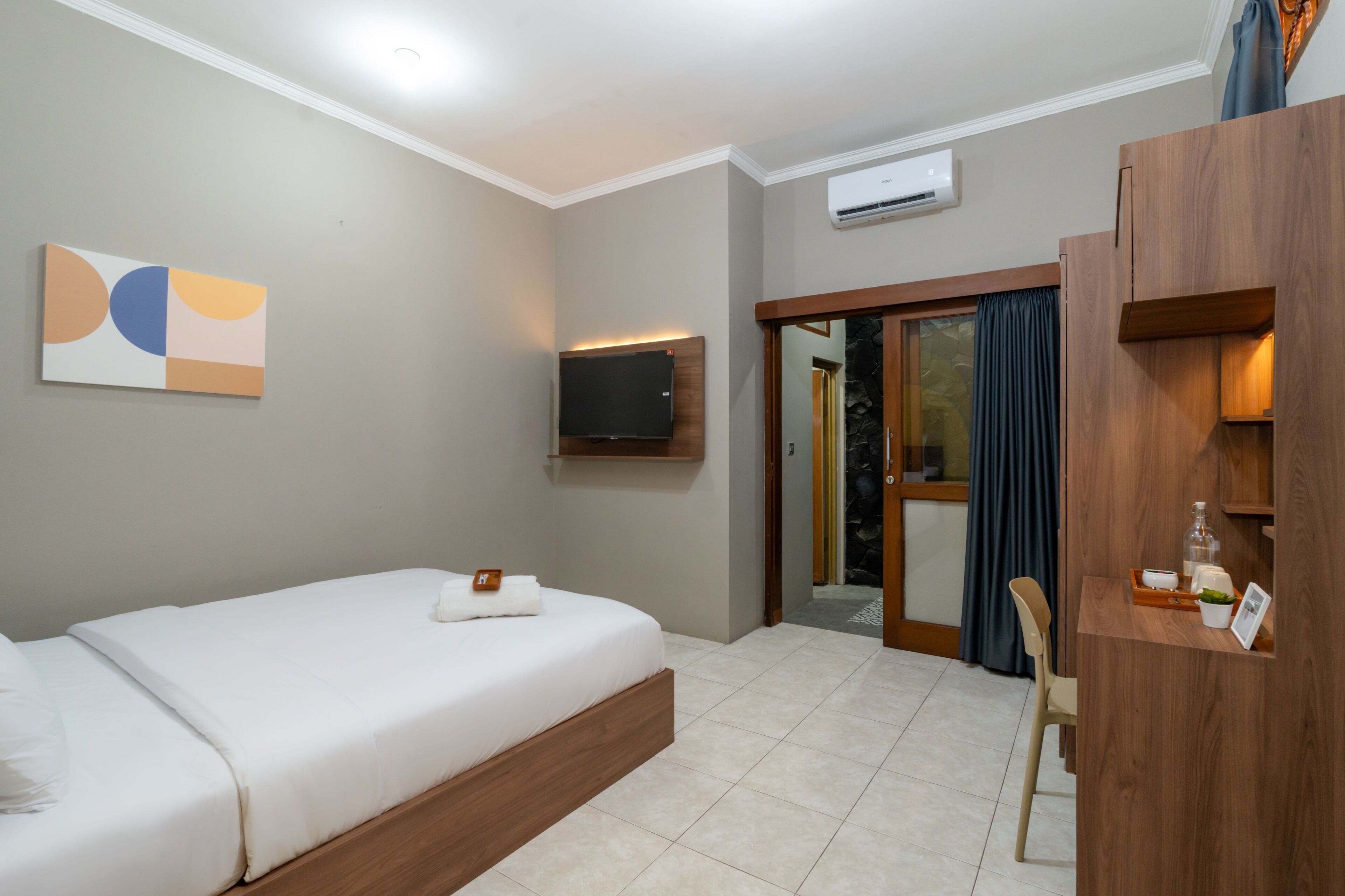 Une chambre d’hôtel moderne équipée d’un lit, d’un téléviseur à écran plat, d’une armoire en bois et d’une porte donnant sur un balcon.