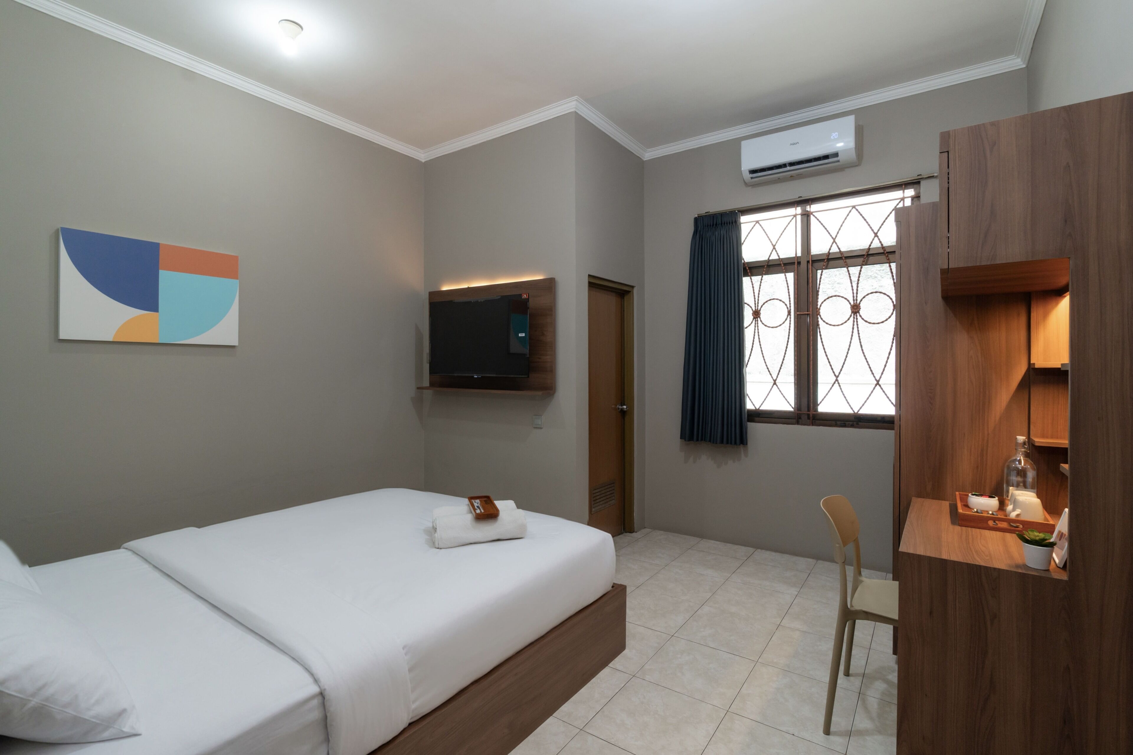 A hotel room with a bed, a desk, a TV, and a window with curtains.