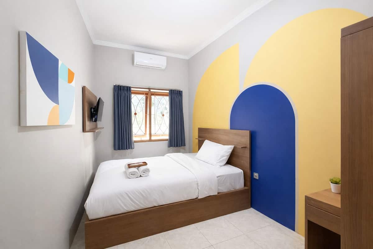 A bedroom with a bed, a TV, a window with curtains, and a wall with a geometric design.