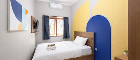 A bedroom with a bed, a TV, a window with curtains, and a wall with a geometric design.