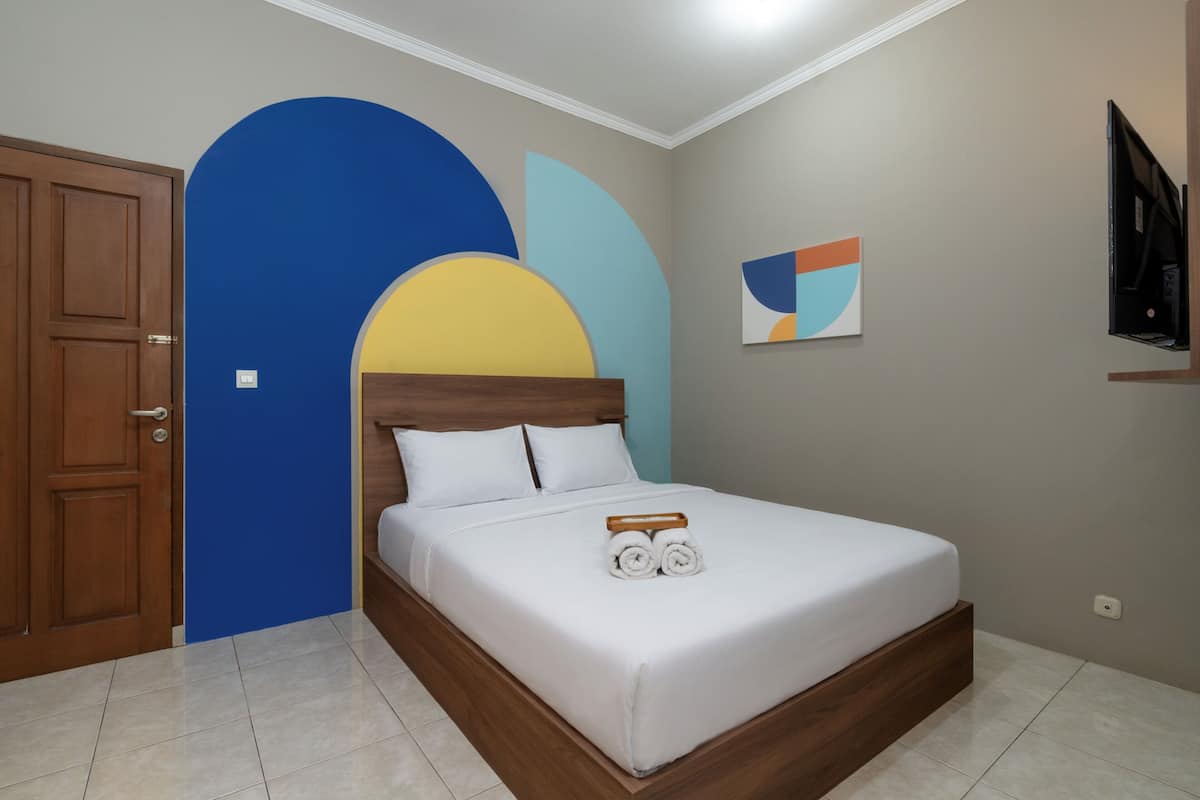 A bedroom with a bed, a wooden door, and a wall with a geometric painting.