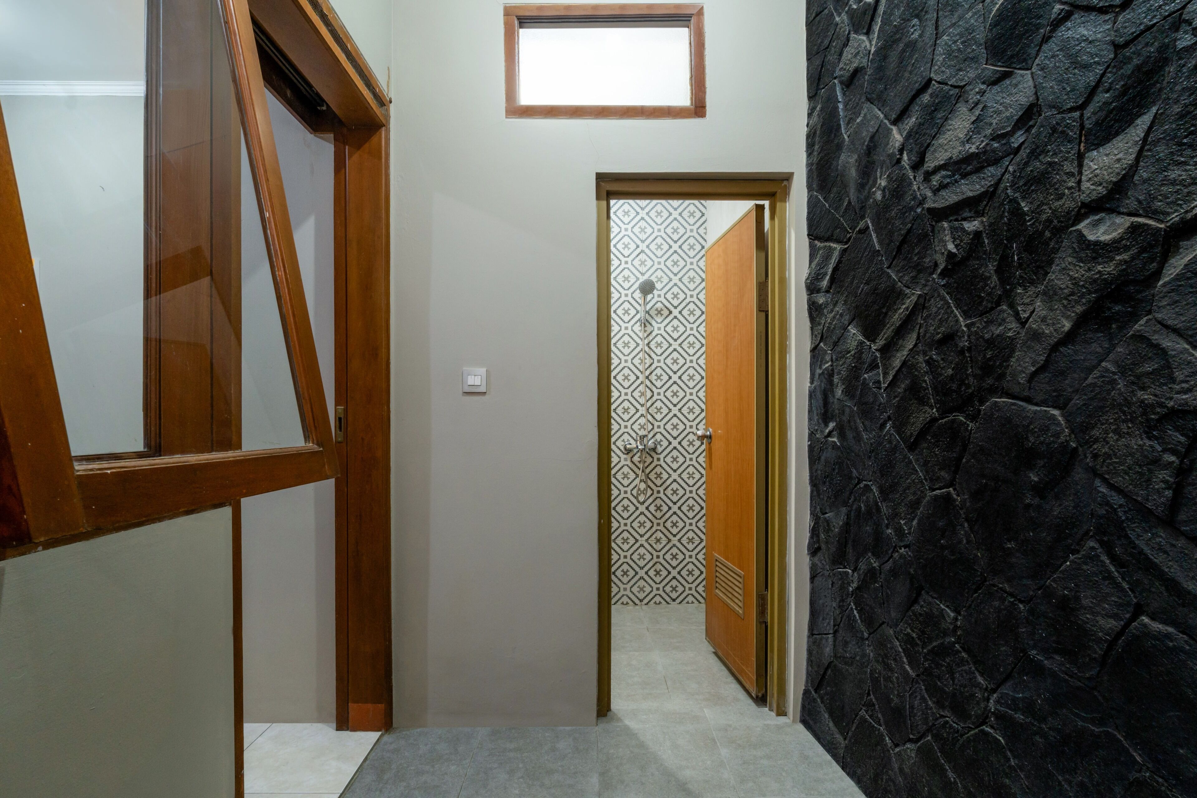 A hallway with a wooden door, a stone wall, and a patterned door in the background.