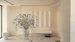Un intérieur moderne avec une table ronde, un vase contenant des fleurs séchées, un banc et un design minimaliste.