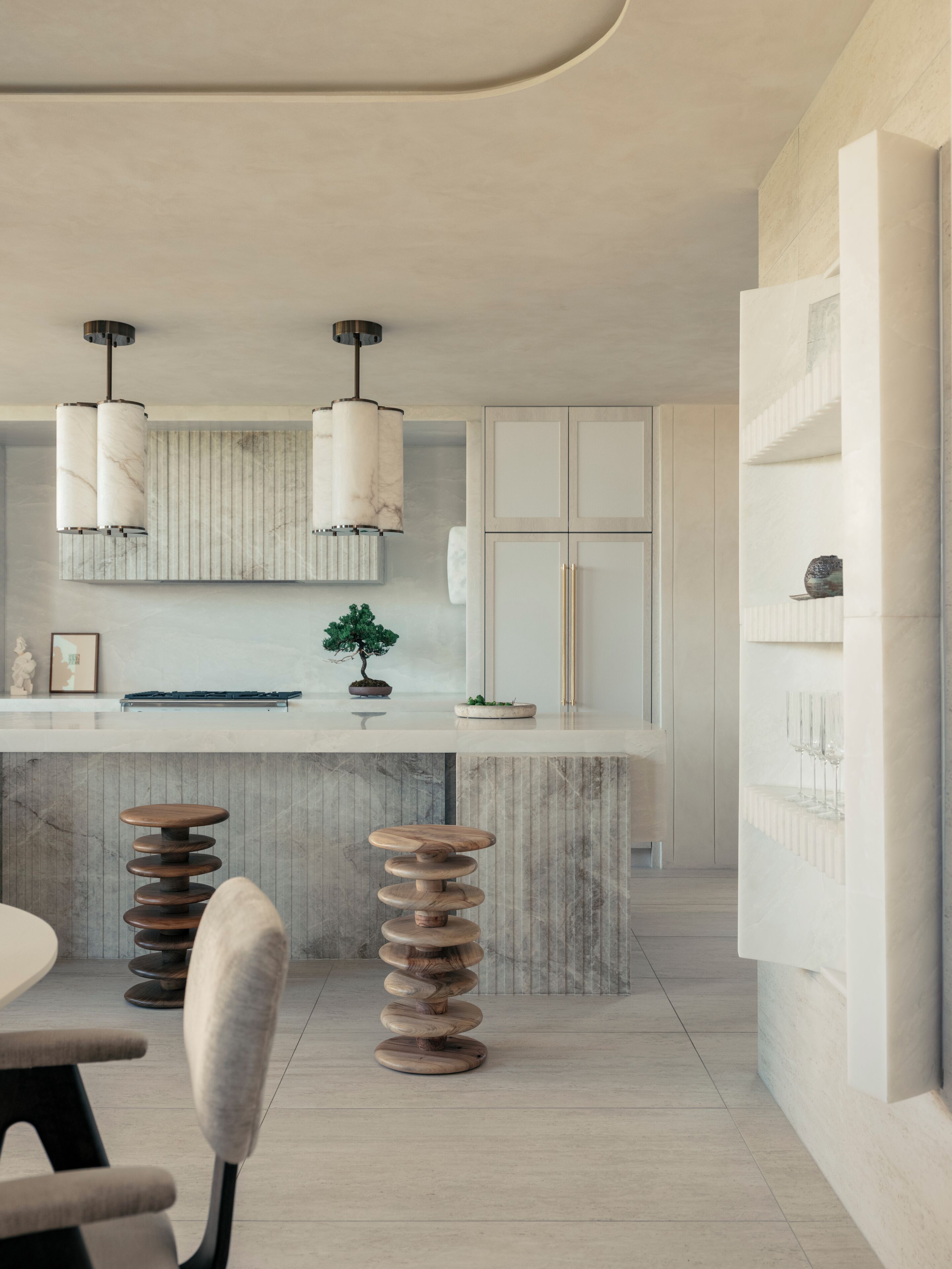 A modern kitchen with a marble countertop, two pendant lights, and a potted plant.