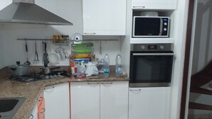 Une cuisine avec des meubles blancs, un four à micro-ondes, un four traditionnel et une cuisinière à gaz.