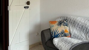 Une pièce avec une porte blanche, un panier tressé accroché à la porte, un canapé gris avec des coussins à motifs et une citation inspirante sur le mur.
