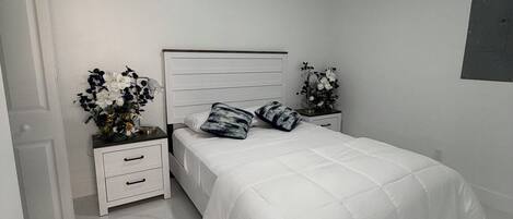 A bedroom with a white bed, two nightstands, a ceiling fan, and a white door.