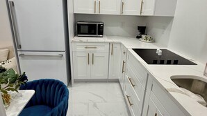 Una cocina moderna con armarios blancos, un microondas negro, un lavamanos y una silla azul.