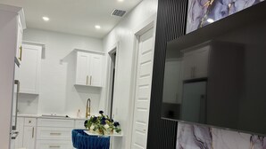 Una sala de estar moderna con un sofá blanco, una mesa de comedor con mantel azul y un televisor montado en la pared.