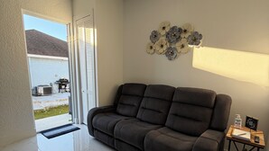 Una sala de estar moderna con un sofá gris oscuro, una mesita de madera con una lámpara y un elemento decorativo en la pared.