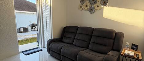 A modern living room with a dark grey sofa, a wooden side table with a lamp, and a decorative wall piece.