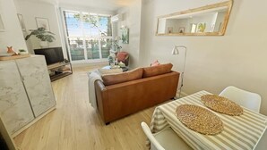 Una sala de estar con un sofá, un televisor, una mesa de comedor con individuales, una lámpara y un ventanal con persianas.