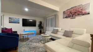 Un salon avec un canapé, un fauteuil bleu, une table basse, un téléviseur et un tableau accroché au mur.