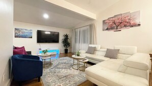 Un salon moderne avec un canapé blanc, un fauteuil bleu, une table basse et un téléviseur fixé au mur.