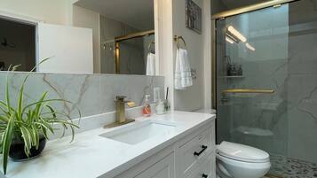 A modern bathroom with a vanity, sink, mirror, and a shower area.