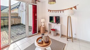 Ein modernes Wohnzimmer mit Schiebeglastür zu einem Balkon, einem Flachbildfernseher, einer Lampe und einem 'VACANCY'-Schild an der Wand.