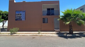 Un edifici de dues plantes amb un balcó, una petita zona de jardí i una palmera.
