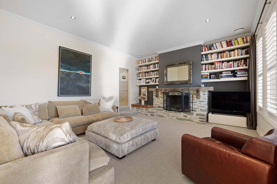 A living room with a sofa, ottoman, fireplace, bookshelf, and a large painting.
