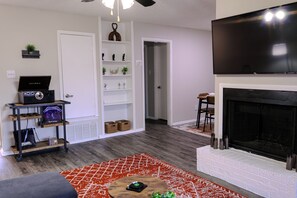 A living room with a fireplace, a TV mounted on the wall, and a bookshelf with decorative items.