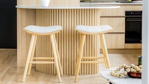 A modern kitchen with a wooden accent wall, two bar stools, a white vase, and a kitchen island. - Medusa Bondi (Bondi)