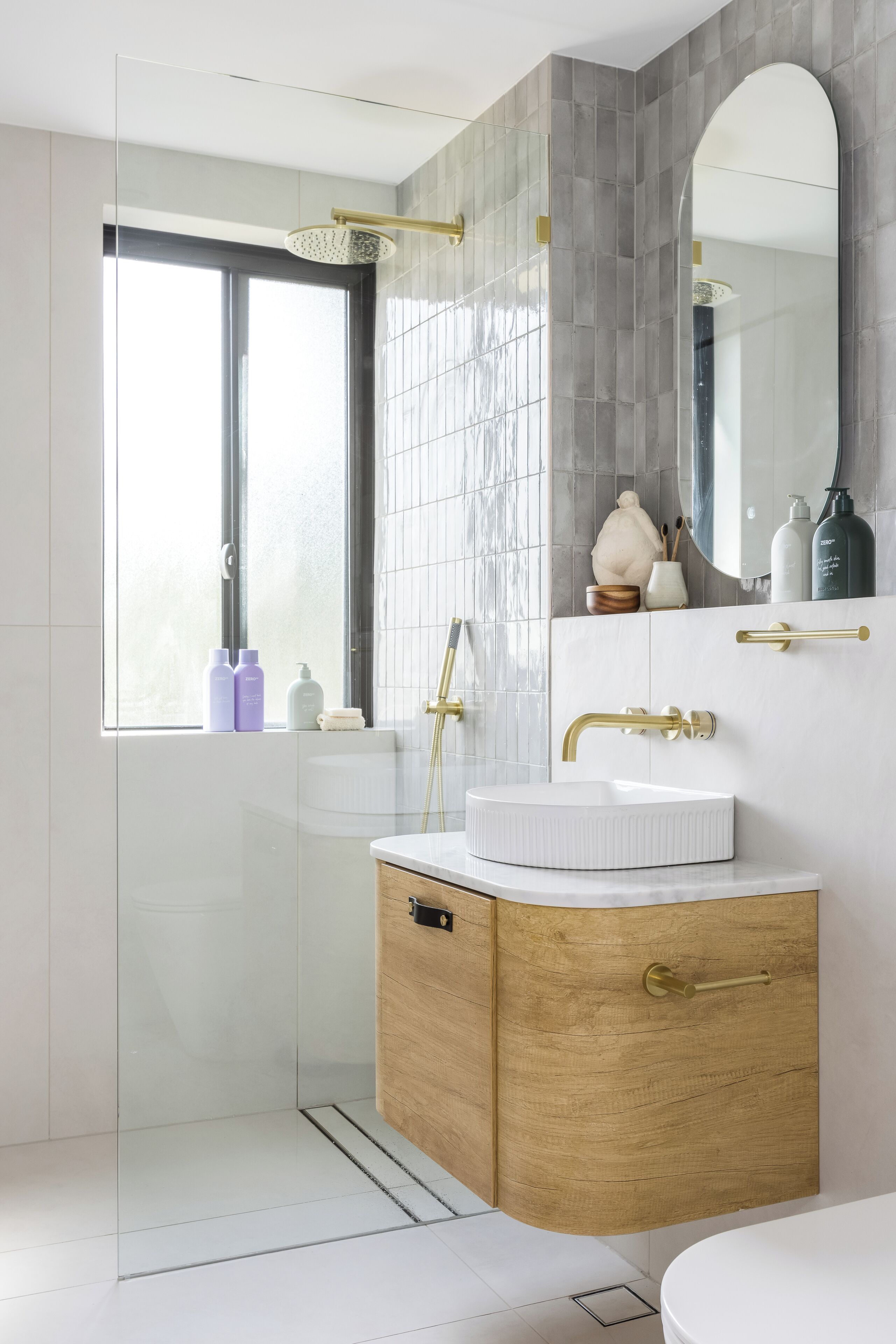 A modern bathroom with a glass shower enclosure, a white sink with a wooden vanity, and a large mirror above the vanity.