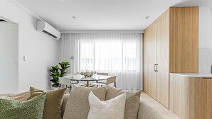 A modern living room with a beige sofa, a dining table, and a kitchen area with wooden cabinets. - Medusa Bondi (Bondi)
