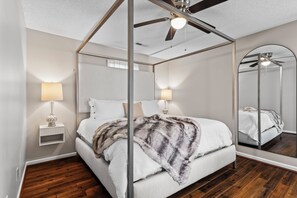 Une chambre à coucher avec un lit à baldaquin, deux lampes de chevet, un ventilateur de plafond et un grand miroir.