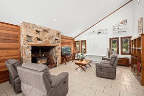 A living room with a stone fireplace, leather sofas, a wooden TV stand, and a white cabinet with glass doors.