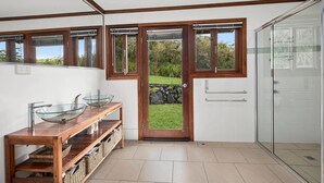 A bathroom with a glass shower, a wooden vanity with a glass bowl sink, and a door leading to a garden.