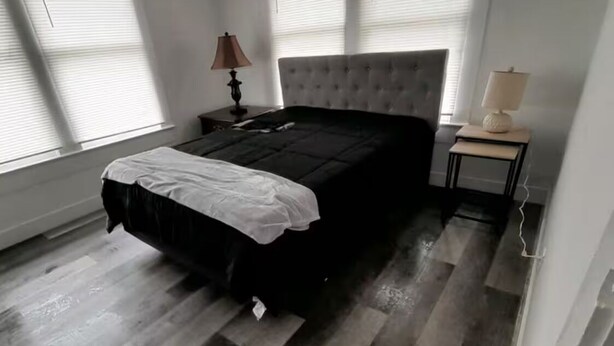 A bedroom with a large bed, two bedside tables with lamps, and a window with blinds.