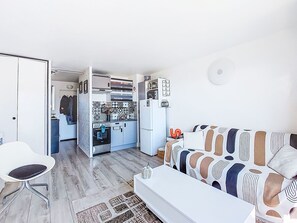 A compact living space with a kitchenette, a white sofa, a white chair, and a patterned rug. - Le Fidji by Interhome (La Ciotat)