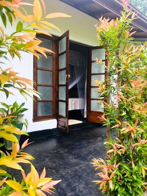 A room with an open door leading to a bed with a mosquito net. - Mashi's Villa (Sigiriya)