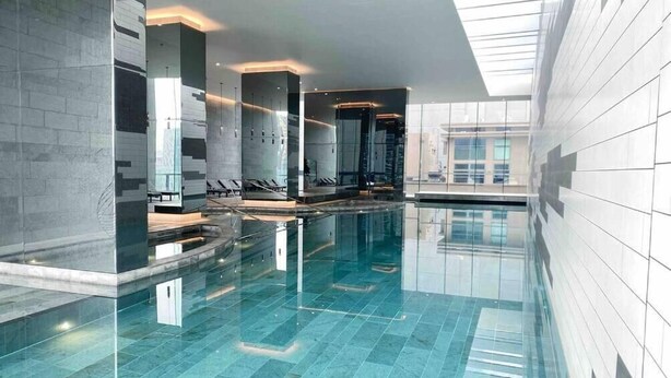 Una piscina interior moderna con paredes de vidrio transparente, suelo de baldosas y diseño elegante.