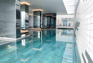 A modern indoor swimming pool with clear glass walls, a tiled floor, and a sleek design. - Puddings Home Sea View Southern Cross Pool Gym (Melbourne)