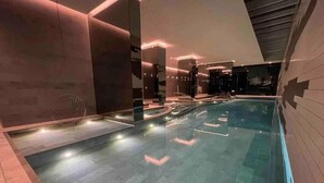 Una piscina interior moderna con iluminación geométrica y vistas claras del horizonte urbano a través de las ventanas.