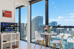 A modern hotel room with a large window, a flat-screen TV, a small table with chairs, and a decorative vase. - Puddings Home Sea View Southern Cross Pool Gym (Melbourne)