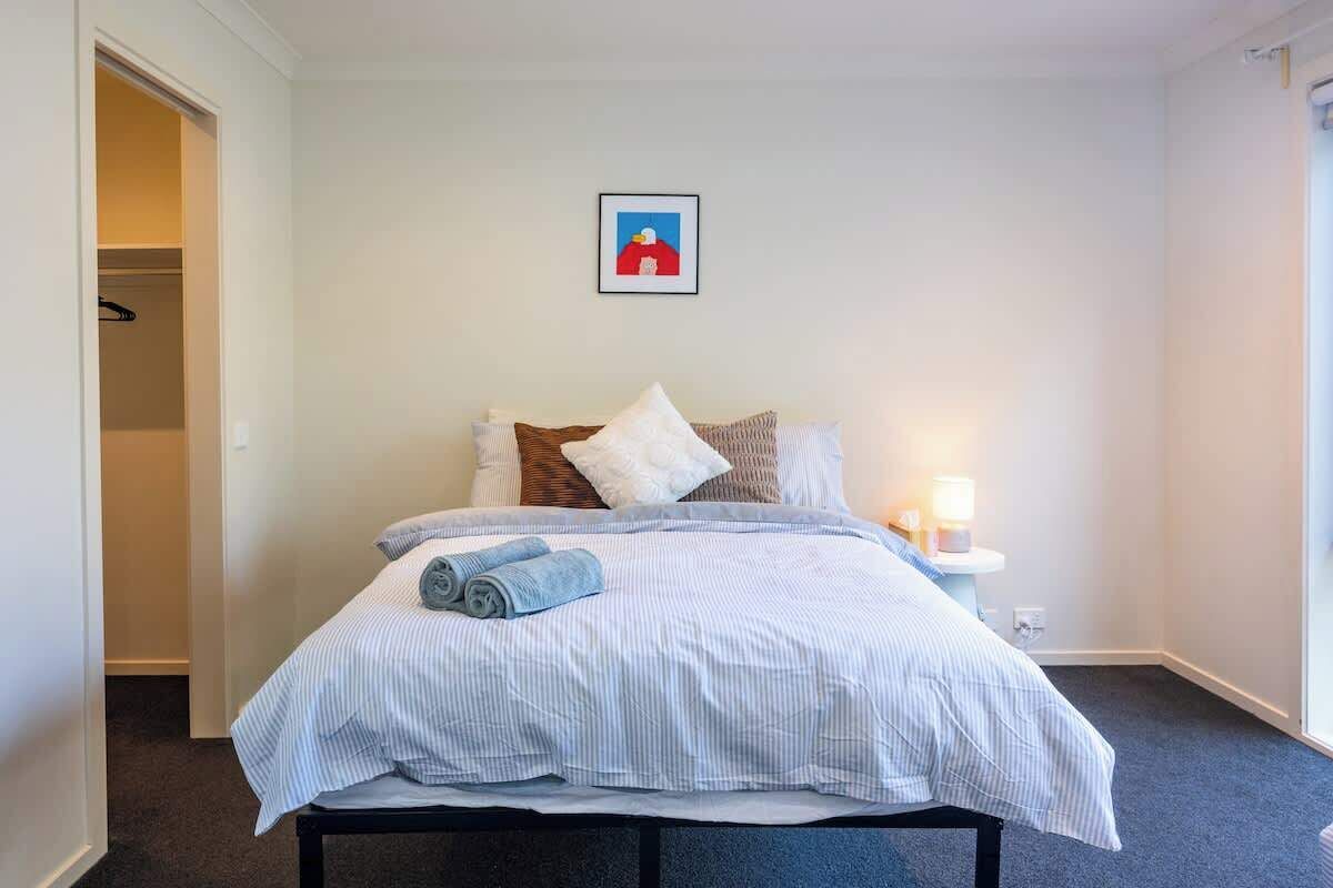 Un lit bien fait, avec une literie à rayures et une serviette enroulée, une lampe de chevet et un tableau encadré au mur.