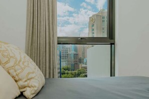 Ein Hotelzimmer mit Bett, Fenster mit Blick auf Stadtgebäude und Vorhang.