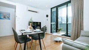 A modern living room with a dining area, large windows with a city view, and a cozy seating area. - 5 Min to Crown & NGV | Stylish 2BR | City View (Southbank)