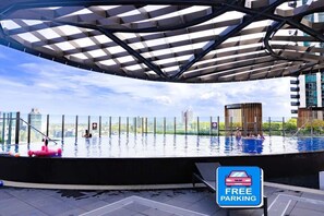 An infinity pool with a view of the city skyline, a covered area with a metal roof, and a sign indicating free parking. - Melbourne Southbank FreeCarPark & Amazing Pool (Southbank)